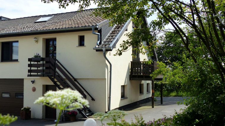 A modern house with a garden and a staircase leading to a balcony. Surrounded by trees and flowers, the environment looks inviting and friendly.