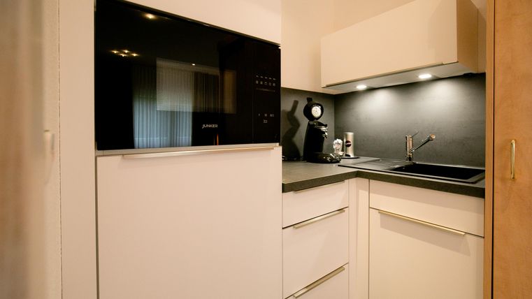 A modern kitchen with white cabinets and a black workspace. There is a refrigerator, a coffee machine, and a sink.