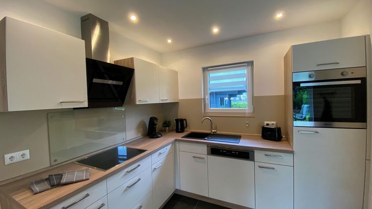 Een moderne keuken met witte kasten en houten details. Ze beschikt over een kookeiland, een fornuis en een ingebouwde oven.