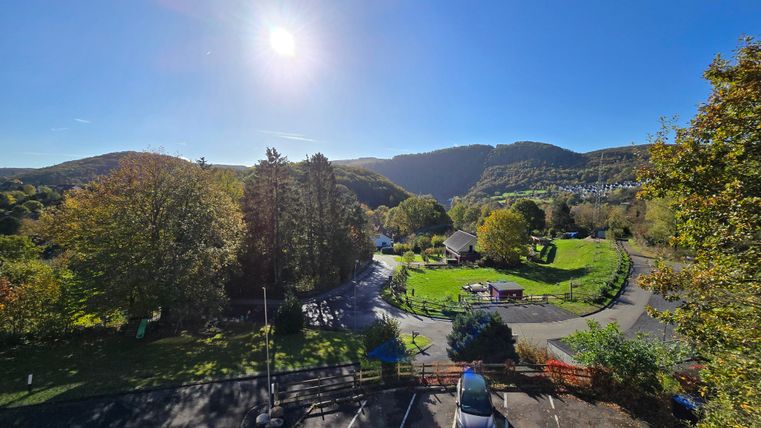 A picturesque landscape with green trees and gentle hills. The sun shines brightly in the blue sky.
