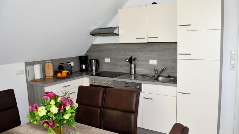 Een moderne keuken met lichte kasten en een eettafel. Op de tafel staat een bloeiende plant en vers fruit.