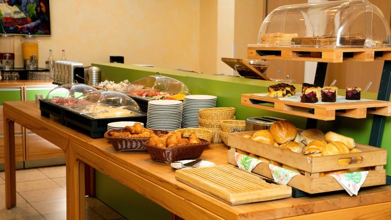 Ein reichhaltiges Frühstücksbuffet mit verschiedenen Broten, Gebäcken und Aufschnitt. Die Speisen sind auf einem Holztablett und in Glasbehältern angerichtet.