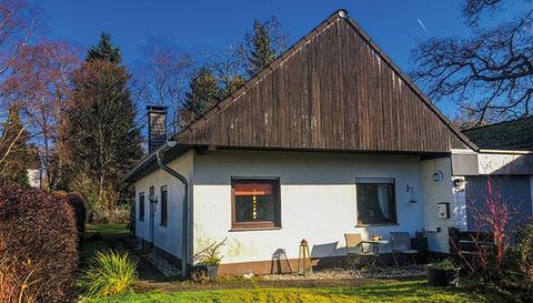Een eenvoudig huis met een hellend dak en een kleine tuin. Het is omringd door bomen en heeft een heldere blauwe lucht op de achtergrond.
