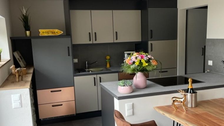Een moderne keuken met grijze en lichte kasten. Op de tafel staat een vaas met kleurrijke bloemen.