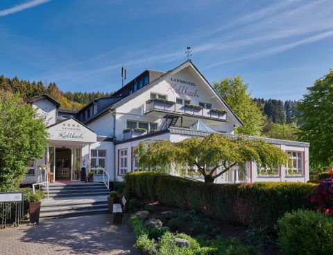 Ein elegantes Hotelgebäude mit Außenanlagen und gut gepflegten Gärten. Der Himmel ist klar und die Umgebung zeigt eine grüne Landschaft.