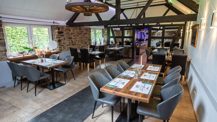 A modern restaurant with wooden beams and elegant tables. The decor is bright and inviting, with large windows that let in plenty of light.