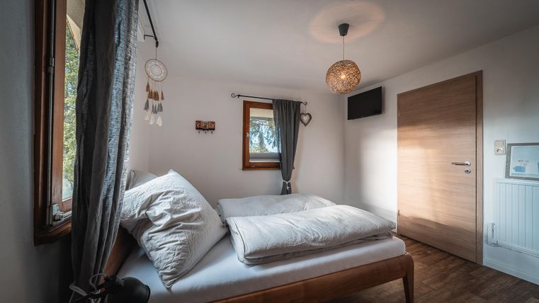 Een gezellig slaapkamer met een tweepersoonsbed en een groot raam. De muren zijn licht, en er zijn decoratieve elementen zoals een dromenvanger.