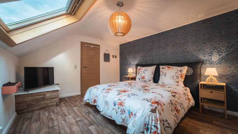 Een moderne slaapkamer met een groot bed en een bloeiende dekbed. De ruimte heeft een televisie, nachtkastjes en een dakraam.