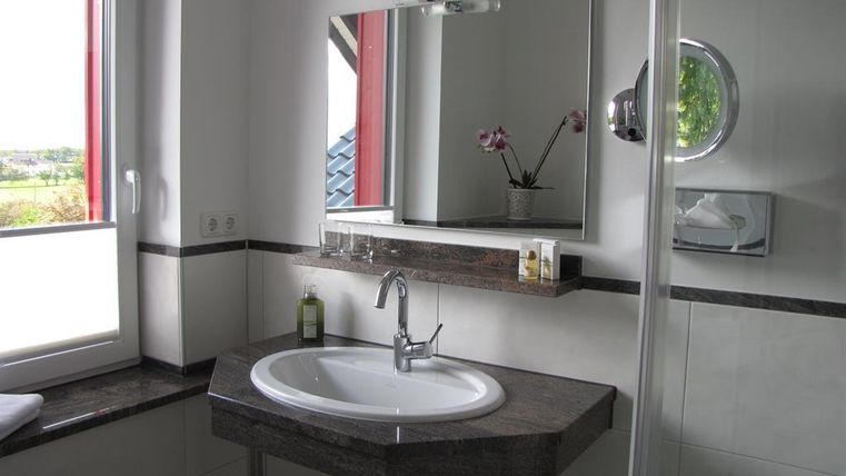 A modern bathroom with a round sink and a large mirror. The windows let in a lot of light and there is an elegant shower area.