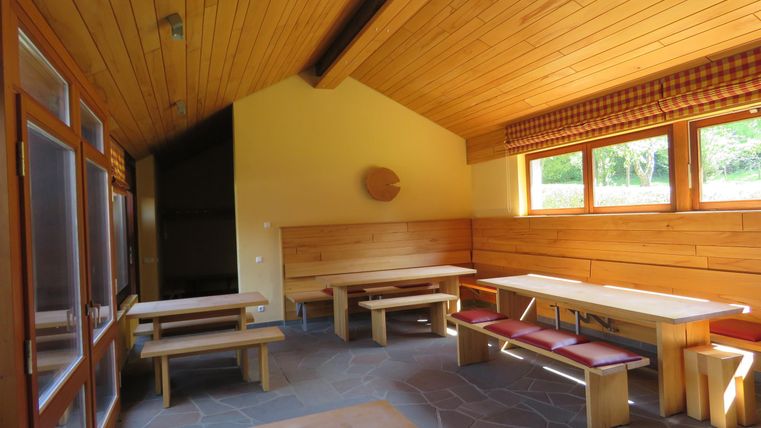 Ein gemütlicher Raum mit Holzwänden und Bänken. Die großen Fenster bieten einen Blick auf die grüne Umgebung.