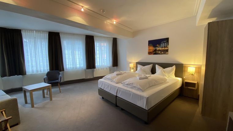 A modern bedroom with two beds and soft lighting. The room is equipped with a table, a chair, and large windows.