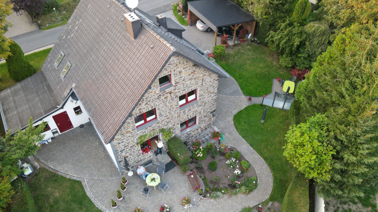 Een mooi huis van steen met een goed onderhouden tuin. Op de voorgrond zijn zithoeken en bloemperken te zien.