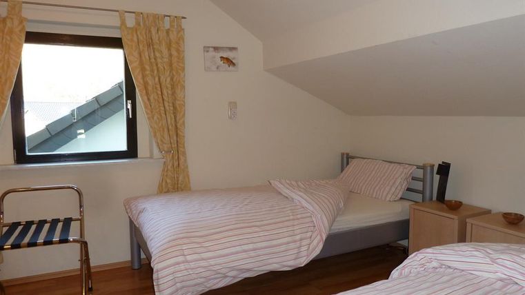 A simple bedroom with two single beds and wooden flooring. The window lets in natural light and there is a metal chair.