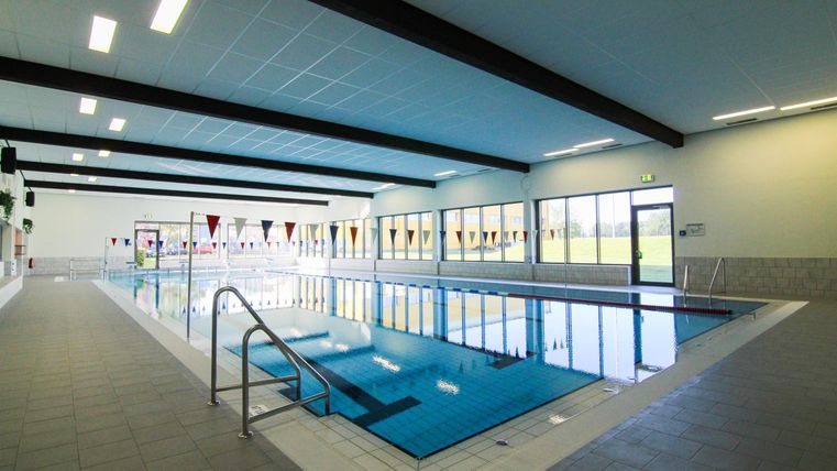 Ein modernes Hallenbad mit einem klaren blauen Wasser. Die großen Fenster sorgen für viel Tageslicht im Raum.