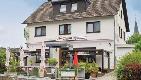 Een gezellige herberg met een terras waar tafels en parasols staan. Op de achtergrond is een rustige plek met groene landschappen te zien.