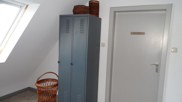 Een lichte kamer met een grijze garderobe en een witte deur. Naast de garderobe staat een gevlochten mand.