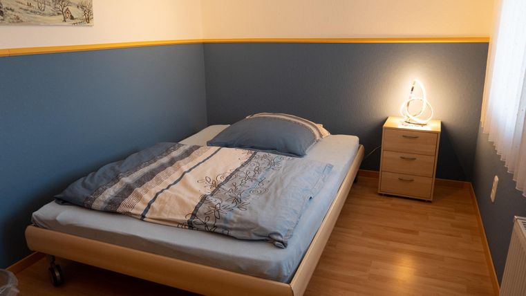 A cozy bedroom with a bed and a nightstand. A blue color is visible on the wall, complemented by a yellow stripe.
