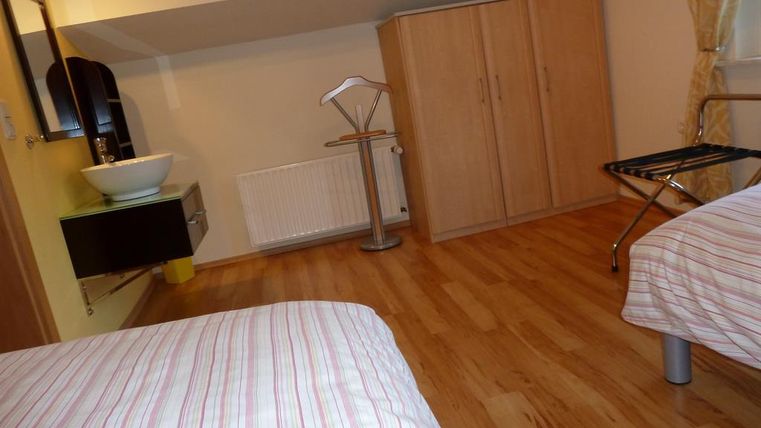 A simple room with two beds and a wooden floor. In the foreground, a sink and a wardrobe are visible.