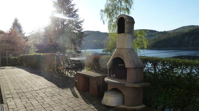 A beautiful outdoor area with a grill and a view of a lake. In the background, nature with trees and gentle hills can be seen.