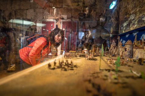 Een persoon in een museum bekijkt een gedetailleerde miniatuurstad. Op de achtergrond zijn historische exposities en standbeelden te zien.
