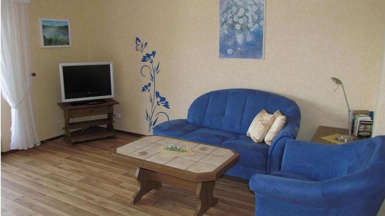 A cozy living room with blue sofas and a television. Decorative floral patterns are on the wall, and the room has a warm ambiance.
