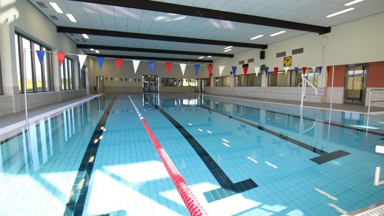 Ein modernes Hallenbad mit klar blauem Wasser. Am Beckenrand sind Schwimmbojen und Lichter angebracht.