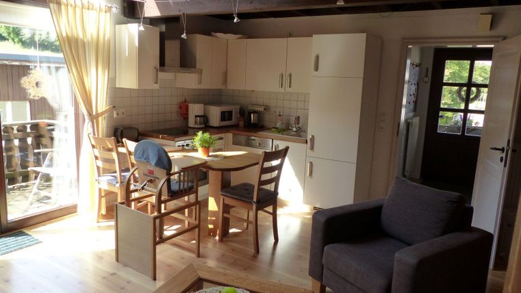 A bright and modern kitchen with a dining area and a cozy armchair. Large windows provide plenty of daylight and create an inviting atmosphere.