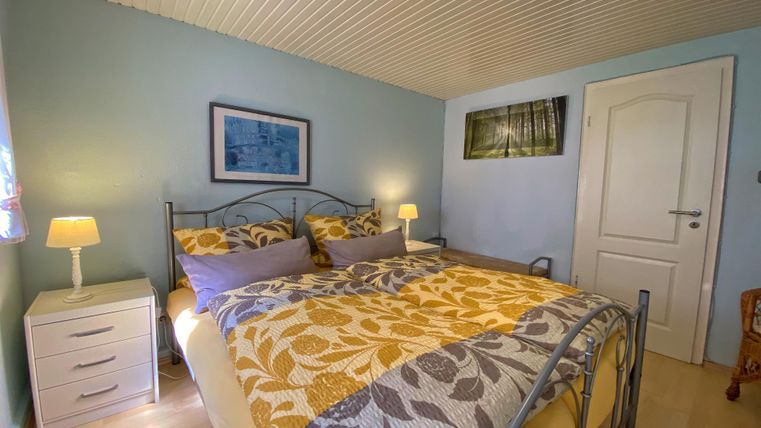 A cozy bedroom with a large bed and colorful pillows. The walls are painted in soft colors and there is a bedside lamp.