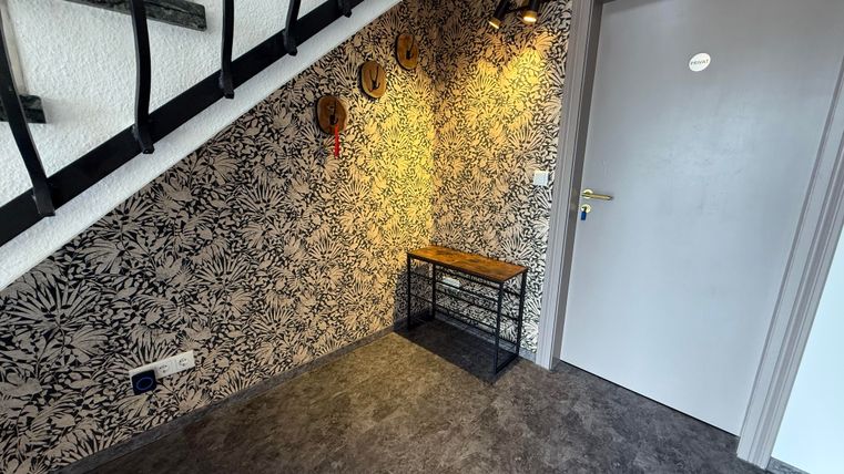 Een moderne gang met een stijlvolle behang en een minimalistisch console. Aan het einde van de gang bevindt zich een grijze deur die de ruimte afsluit.