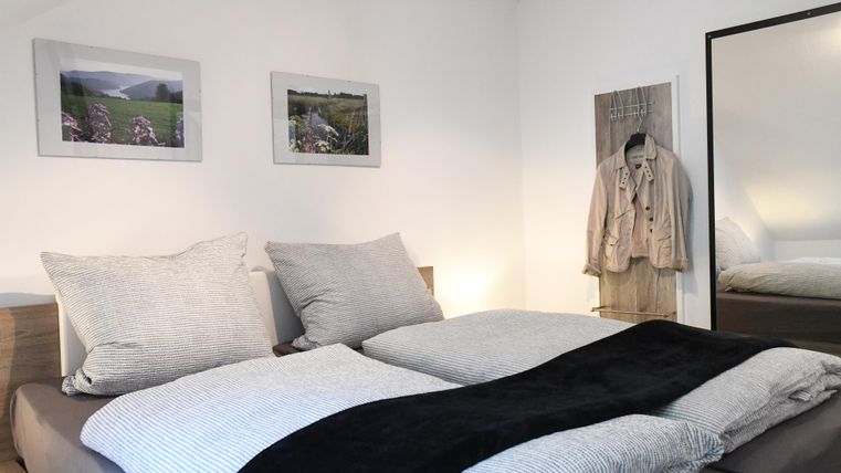 A cozy bedroom with a large bed and soft pillows. Pictures hang on the wall, and a mirror stands next to the bed.