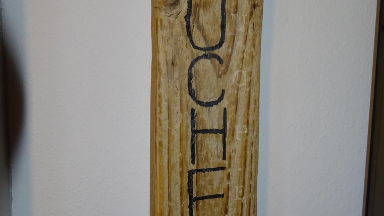 Een houten bord met het woord "KEUKEN" in grote letters. Het bord is aan een muur bevestigd.