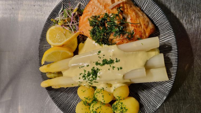 A plate with grilled salmon, asparagus, and small potatoes. Lemon slices and fresh herbs are used for decoration.