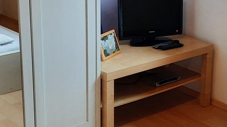 A simple room with a wooden desk and a black television. Next to the television, there is a picture frame on the table.
