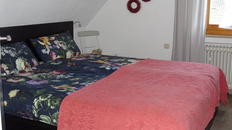 Een gezellig slaapkamer met een groot bed en kleurrijke beddengoed. De muren zijn versierd met decoratieve elementen en er komt veel daglicht binnen.