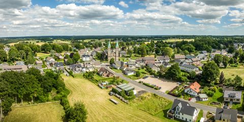Een rustige landschap met een klein dorp en een kerk in het centrum. Rondom het dorp zijn er groene velden en bomen.