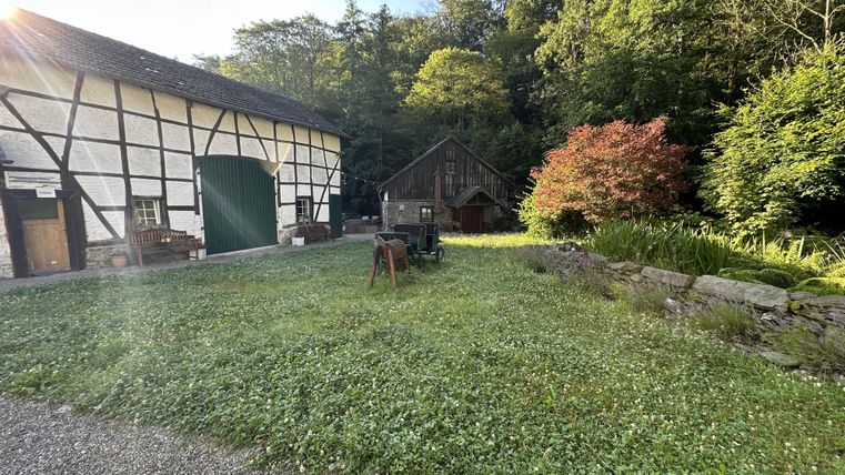 Een idyllische boerderij met een oud vakwerkhuis en een gezellige schuur. De groene tuin is omringd door bomen en bloemen.