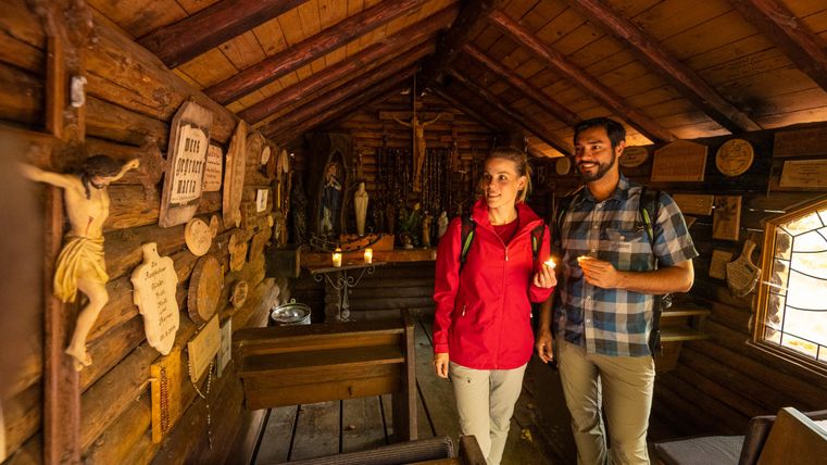 A cozy wooden room with religious figures and decorations. Two people are smiling and exploring the surroundings.