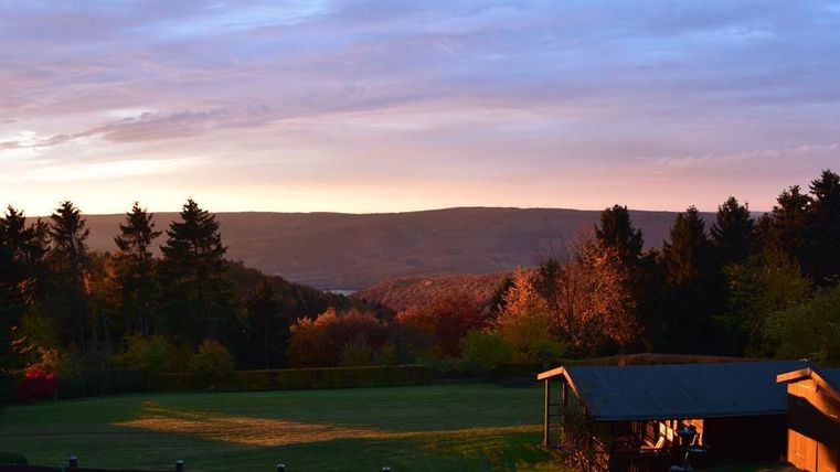 Een schilderachtig landschap met zachte heuvels en bomen bij zonsondergang. De lucht heeft warme kleuren die het tafereel verlichten.
