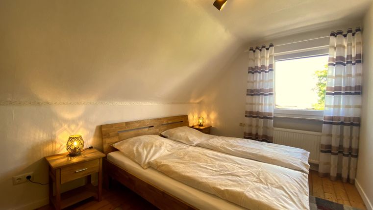 Een gezellige slaapkamer met twee eenpersoonsbedden en warm licht. De grote ramen laten veel daglicht binnen en bieden uitzicht naar buiten.