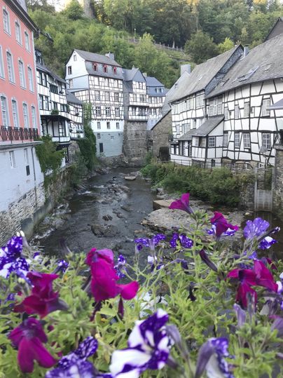 Een schilderachtig oud stadscentrum met vakwerkhuizen aan de rivier. Kleurige bloemen op de voorgrond geven de scène een vrolijke accent.