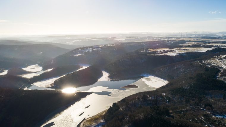 A picturesque landscape with gentle hills and a sparkling body of water. The sky is clear and the sun is shining brightly.