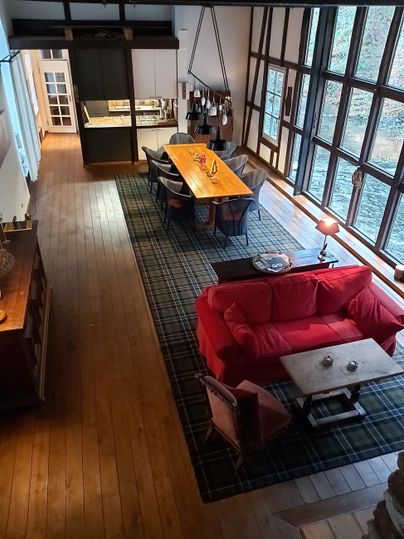 A modern living room with a red sofa and a large wooden table. Large windows let in a lot of light and offer a view of the outdoors.