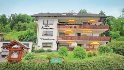 Een gezellig huis met de naam "Panoorama", dat vakantieappartementen aanbiedt. De gevel is omgeven door groene struiken en gele parasols.