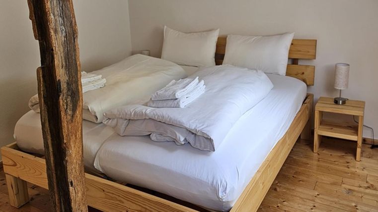 A cozy bedroom with a wooden bed and cheerful white bedding. Next to the bed is a small nightstand with a lamp.