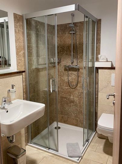 A modern bathroom with a glass shower enclosure. There is a sink and a toilet, surrounded by elegant tiles.