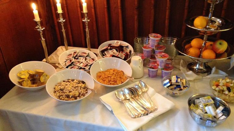A decorated table with various breakfast options, including muesli, fruit, and yogurt. Candles and cutlery add an inviting atmosphere to the arrangement.